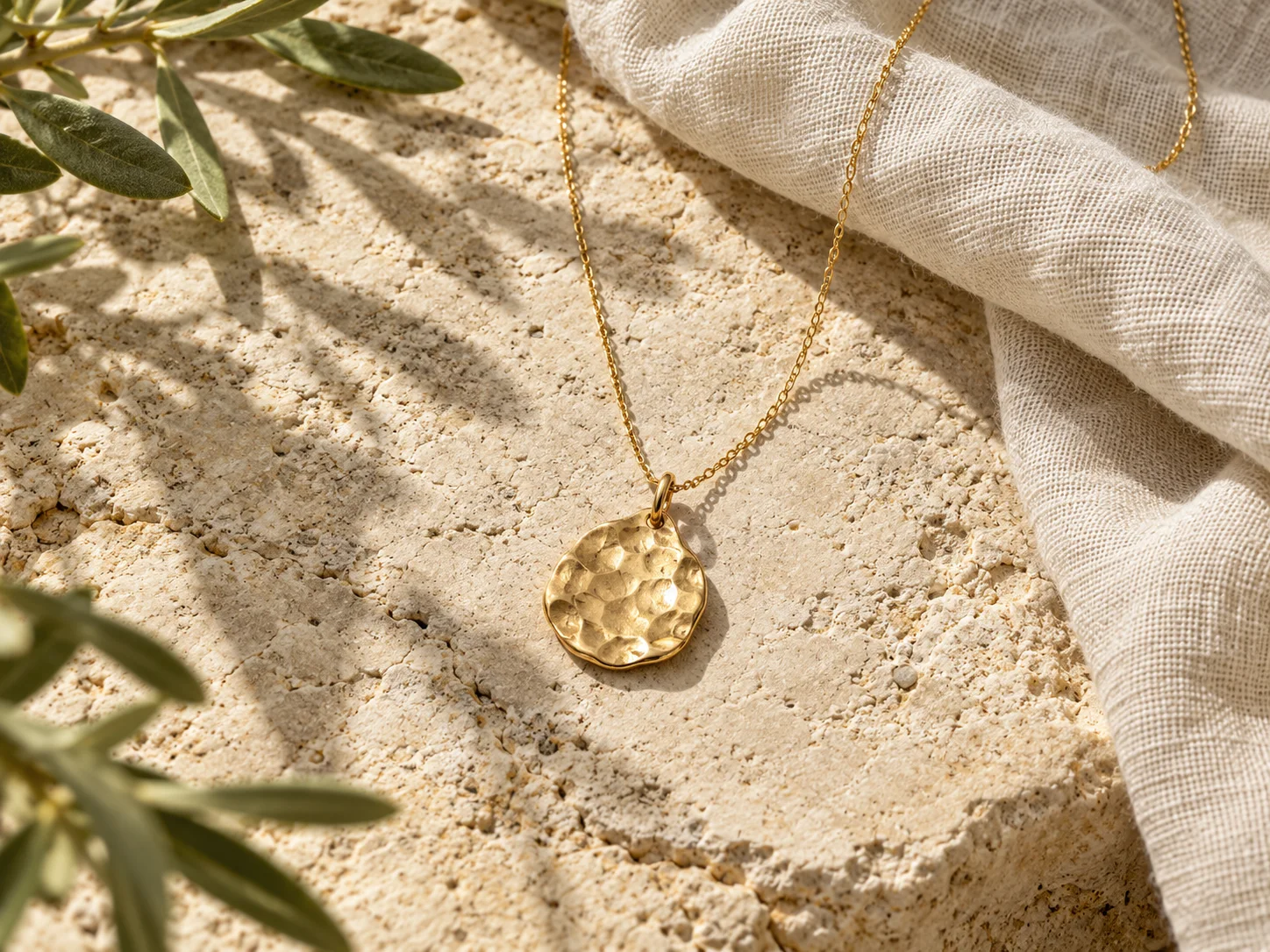 Hammered gold pendant styled on pale limestone and natural linen
